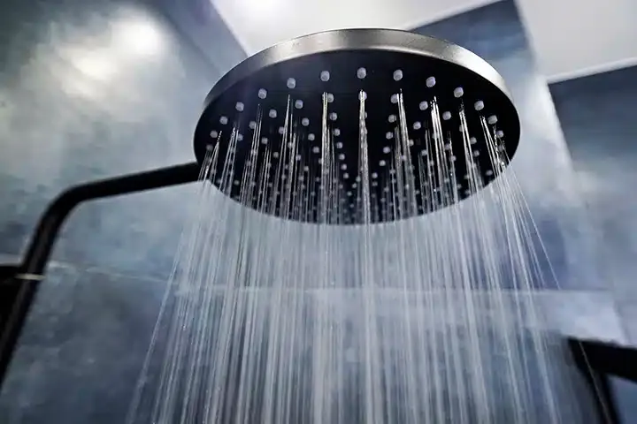 Shower head with water flowing out of it in residential bathroom in Monroe Township, NJ.