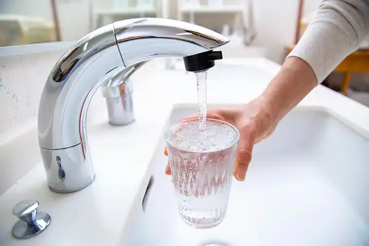 Person filling up water glass in kitchen sink in Monroe Township, NJ.