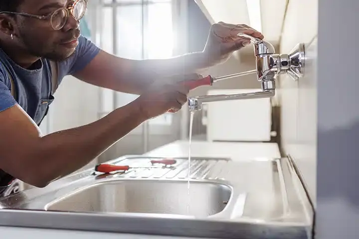 Man fixing kitchen sink faucet leak in Monroe Township, NJ.