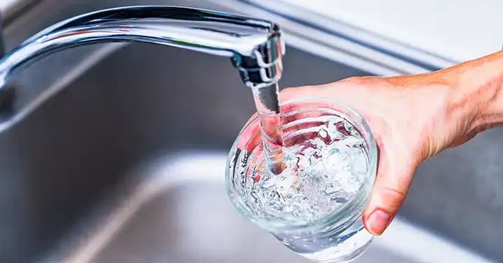 Kitchen sink faucet pouring water into cup